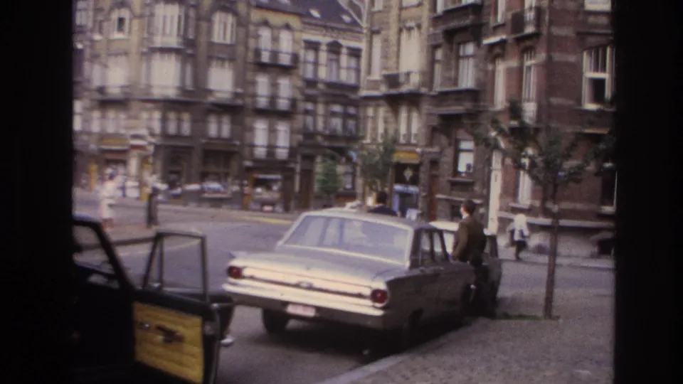 1967 Paris curbside view of a light-colored sedan, open car door, pedestrians, and older apartment facades across the street.