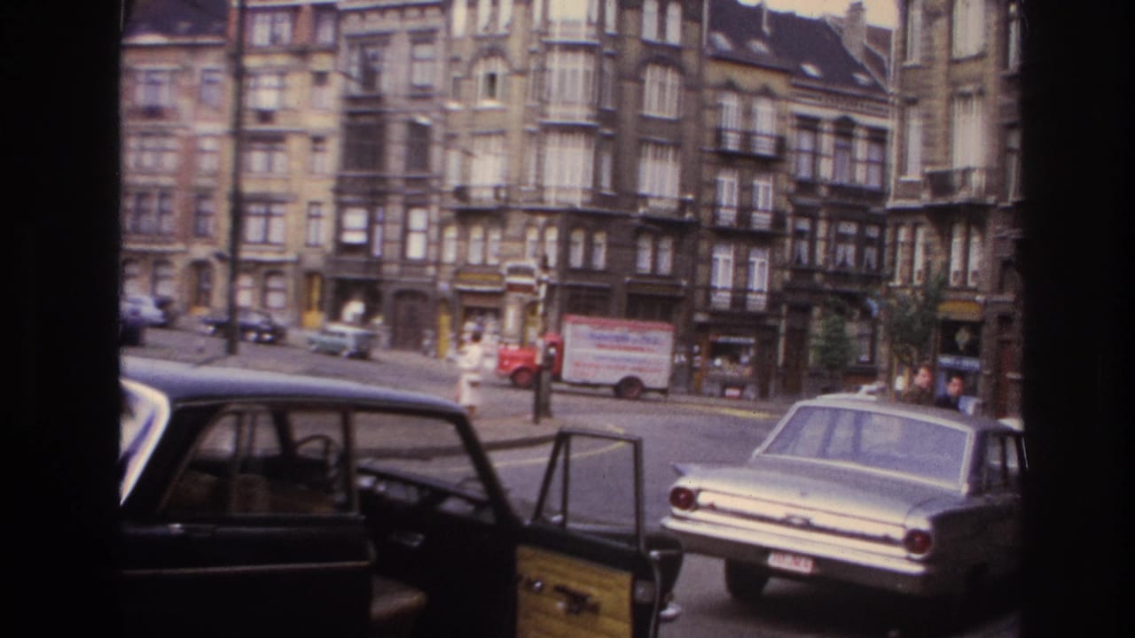 1967 Paris street view from 8mm footage with ornate apartment facades, period cars, and an open foreground car door.