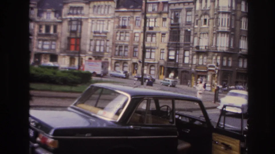 1967 Paris street footage showing a parked car with open door, traffic, greenery, and multi-story apartment buildings.