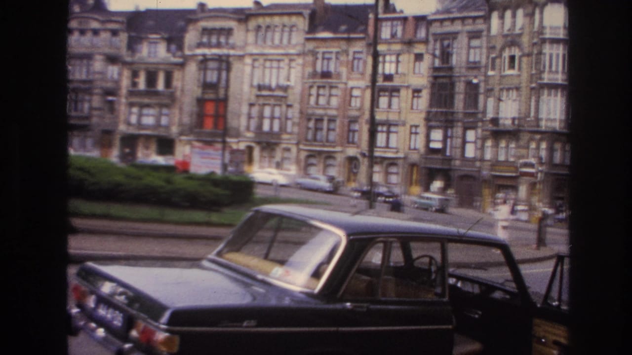 1967 Paris street view from 8mm footage showing a black sedan in the foreground and rows of ornate apartment buildings beyond.