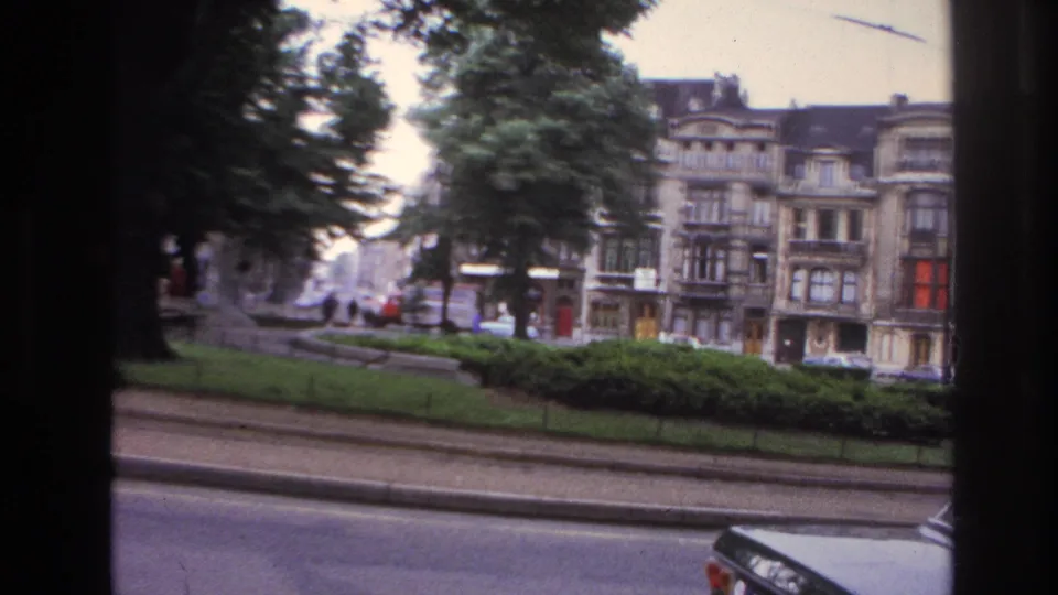 A 1967 Paris roadside view shows trees, hedges, distant cars, and apartment facades from a moving home-movie camera.