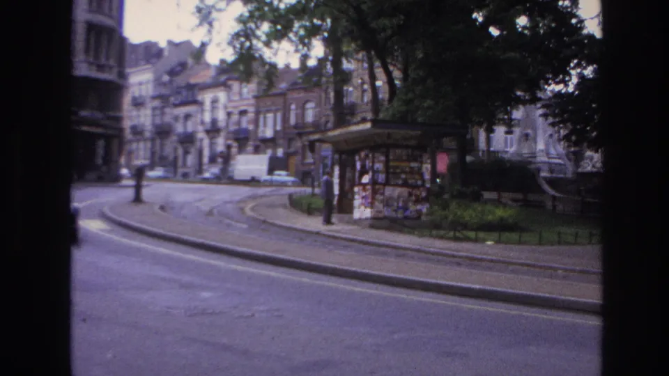 1967 Paris street footage shows the vehicle passing a kiosk beside tram tracks, with trees and apartment buildings softened by motion blur.