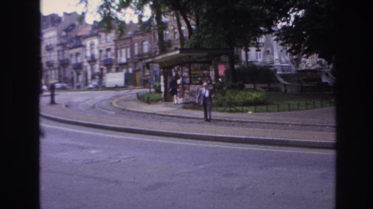 1967 Paris street-side park view with a kiosk, tram tracks, apartment buildings, trees, and an adult man near the curb.