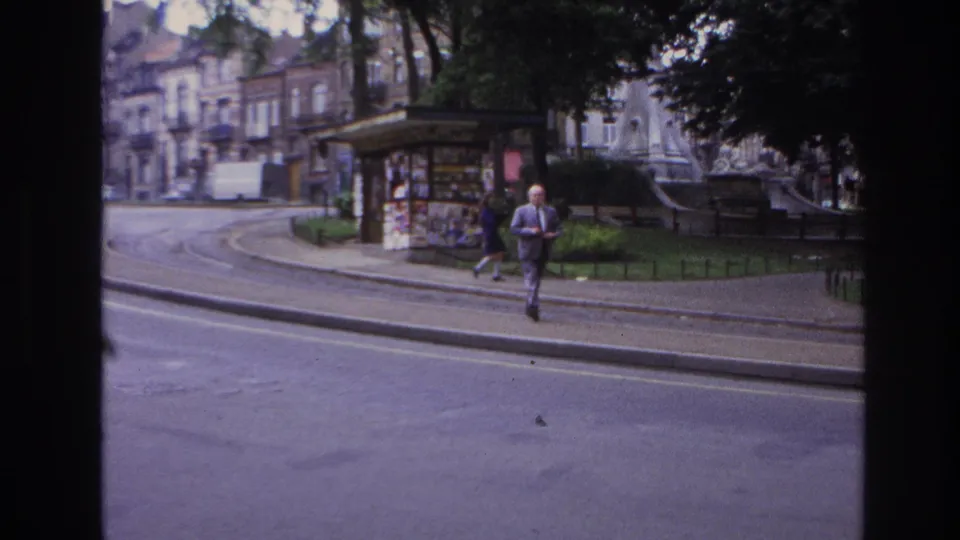 Final frame of the 1967 Paris street scene, with an adult man crossing the foreground sidewalk and a woman near the kiosk behind him.