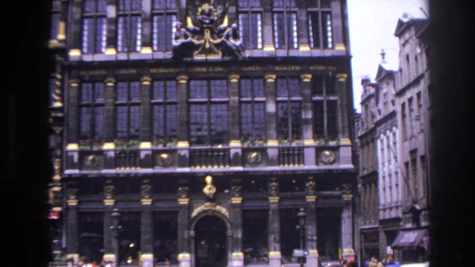 Paris building exterior with gilded architectural details, rows of windows, and street activity below.