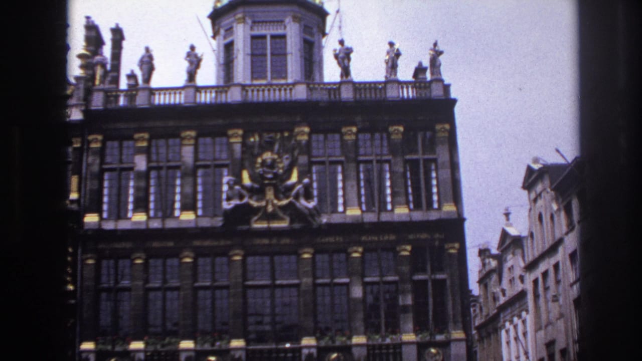 1967 Paris home-movie frame showing an ornate historic facade with tall windows, gilded details, rooftop statues, and dark film borders.