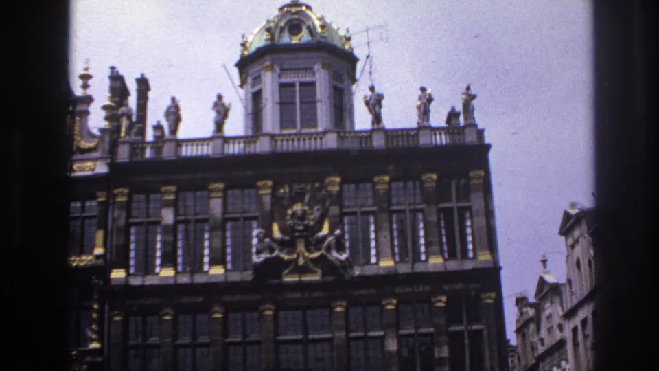 1967 Paris travel footage frame showing the upper portion of an ornate facade, a green-tiled dome, roof statues, and adjoining buildings.