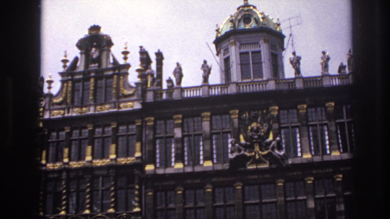 1967 travel-film frame showing an ornate historic facade with gold accents, rooftop statuary, and tall window bays.