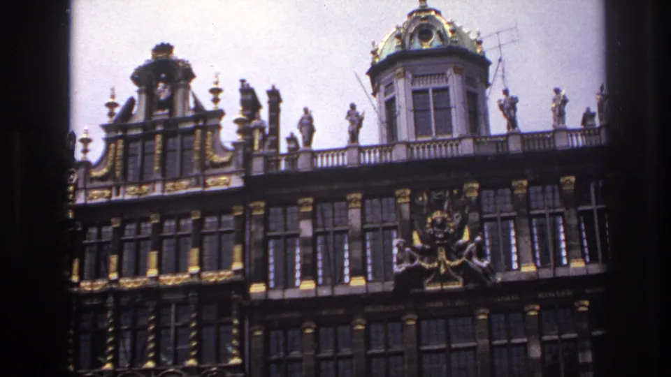 1967 travel-film frame showing an ornate historic facade with gold accents, rooftop statuary, and tall window bays.