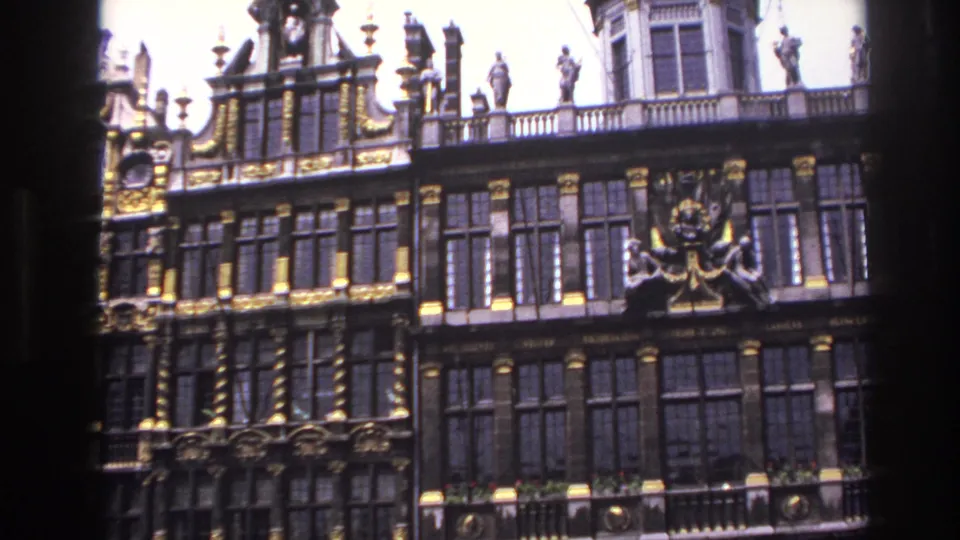 1967 8mm frame of an ornate historic facade, slightly tilted, with gilding, statuary, windows, and balcony rails.