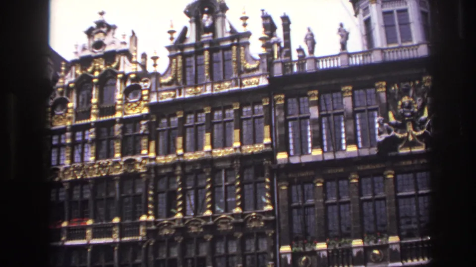 1967 travel-film frame showing a historic facade with gilded details, rooftop statues, window bays, and visible film-edge shadow.