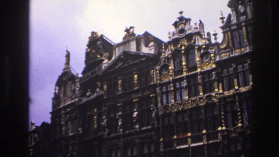 1967 France-linked 8mm frame looking upward at historic facades with gilded decoration, steep gables, and a dark vertical foreground edge.