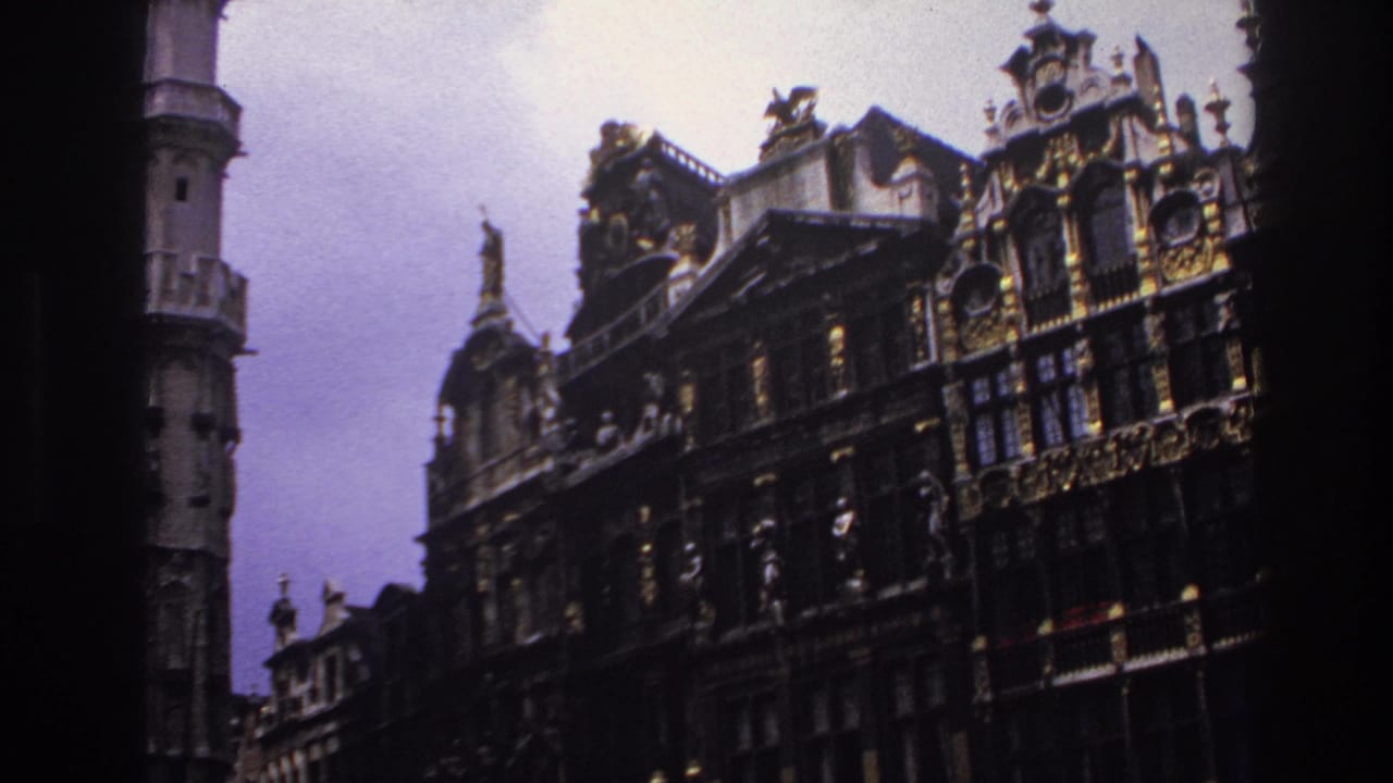 1967 Paris home-movie frame showing ornate historic facades, a pale sky, and a tall stone tower partly blocked by dark framing.