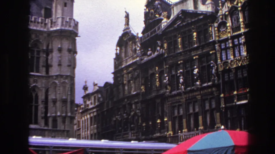 1967 Paris home-movie view of a stone tower and adjacent ornate facades, framed by dark edges with a red-blue umbrella at the lower right.