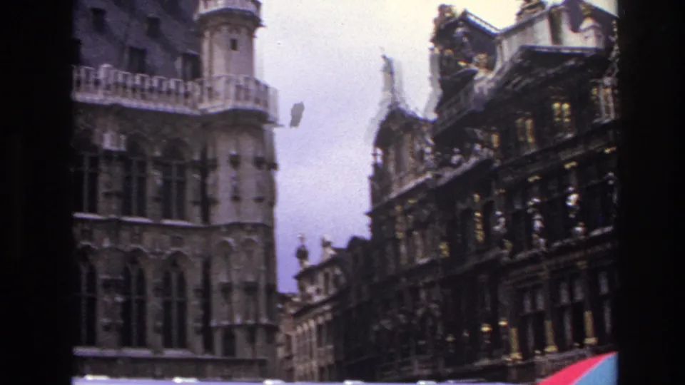 1967 Paris frame showing a tall stone tower, dark ornate facade, rooftop decoration, and a red-blue umbrella edge near the bottom.