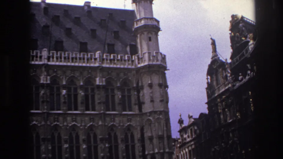Paris 1967 8mm frame of a pale historic facade with arched windows, tower details and adjacent ornate roofline sculpture.
