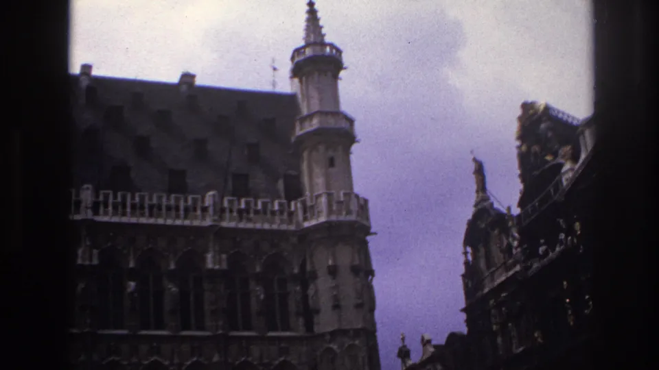 Handheld 1967 Paris travel frame showing historic architecture from below, with tower, roofline and carved facade details.