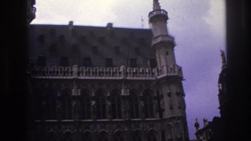 1967 Paris home-movie frame showing a Gothic-style stone facade, steep roof, and turret-like tower partly obscured by dark foreground edges.