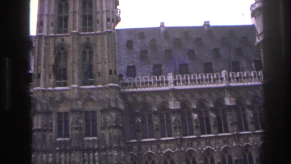 1967 Paris travel frame showing a tall stone tower beside a steep roof and rows of arched windows, with soft 8mm color and grain.