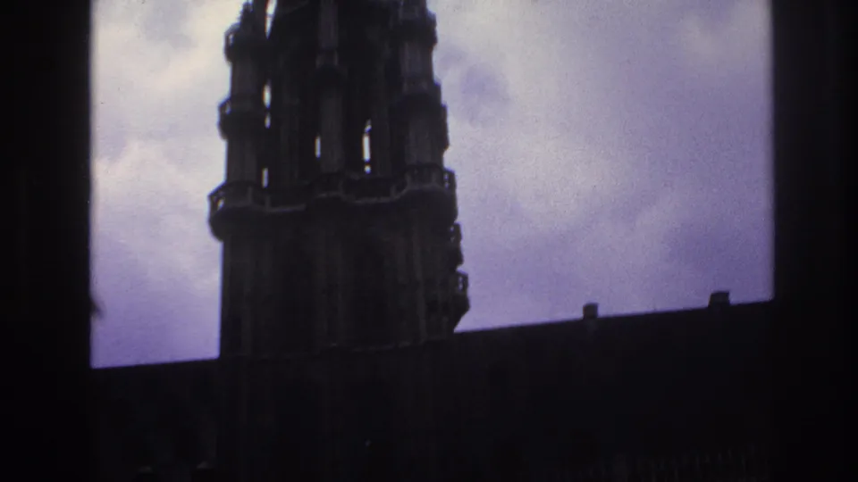 1967 Paris frame with a Gothic cathedral tower and roofline falling into silhouette against a pale cloudy sky.