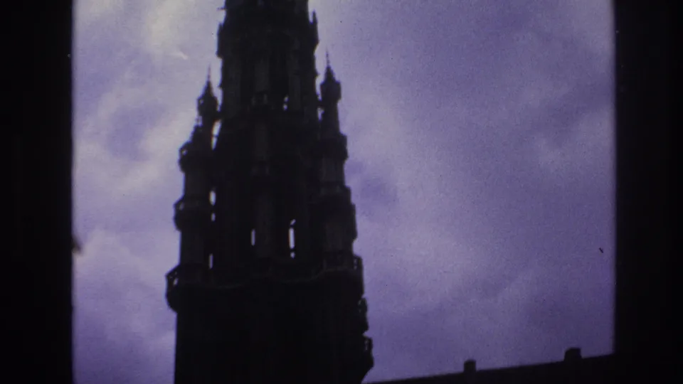 1967 Paris home-movie still showing a tall Gothic spire and upper tower silhouetted against clouded sky.
