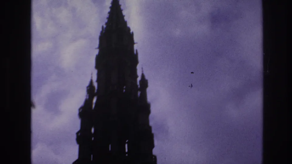 1967 Paris frame centering a pointed Gothic spire in silhouette, with soft clouds and visible film specks.