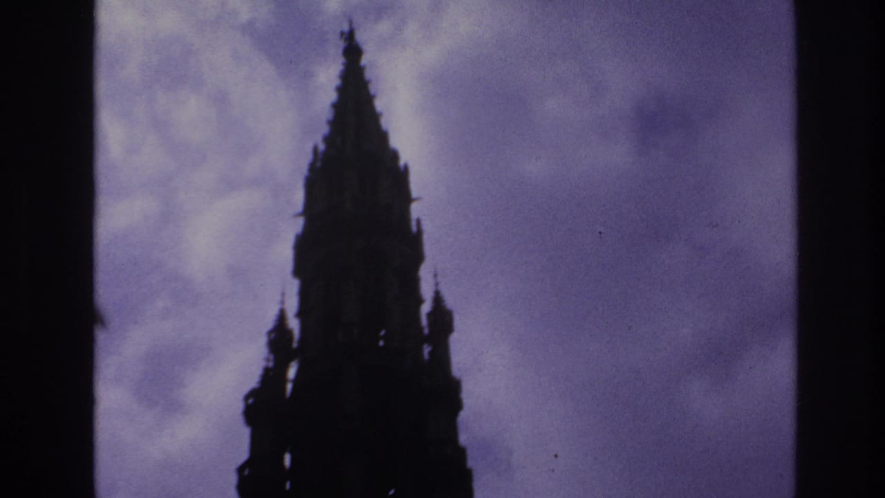 1967 Paris home-movie frame showing a Gothic cathedral spire in dark silhouette against a saturated purple-blue sky.