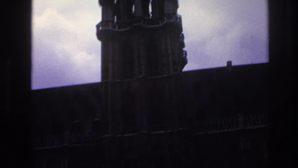1967 Paris frame showing a dark Gothic tower, adjacent roofline, and clouded purple-blue sky in grainy 8mm color.