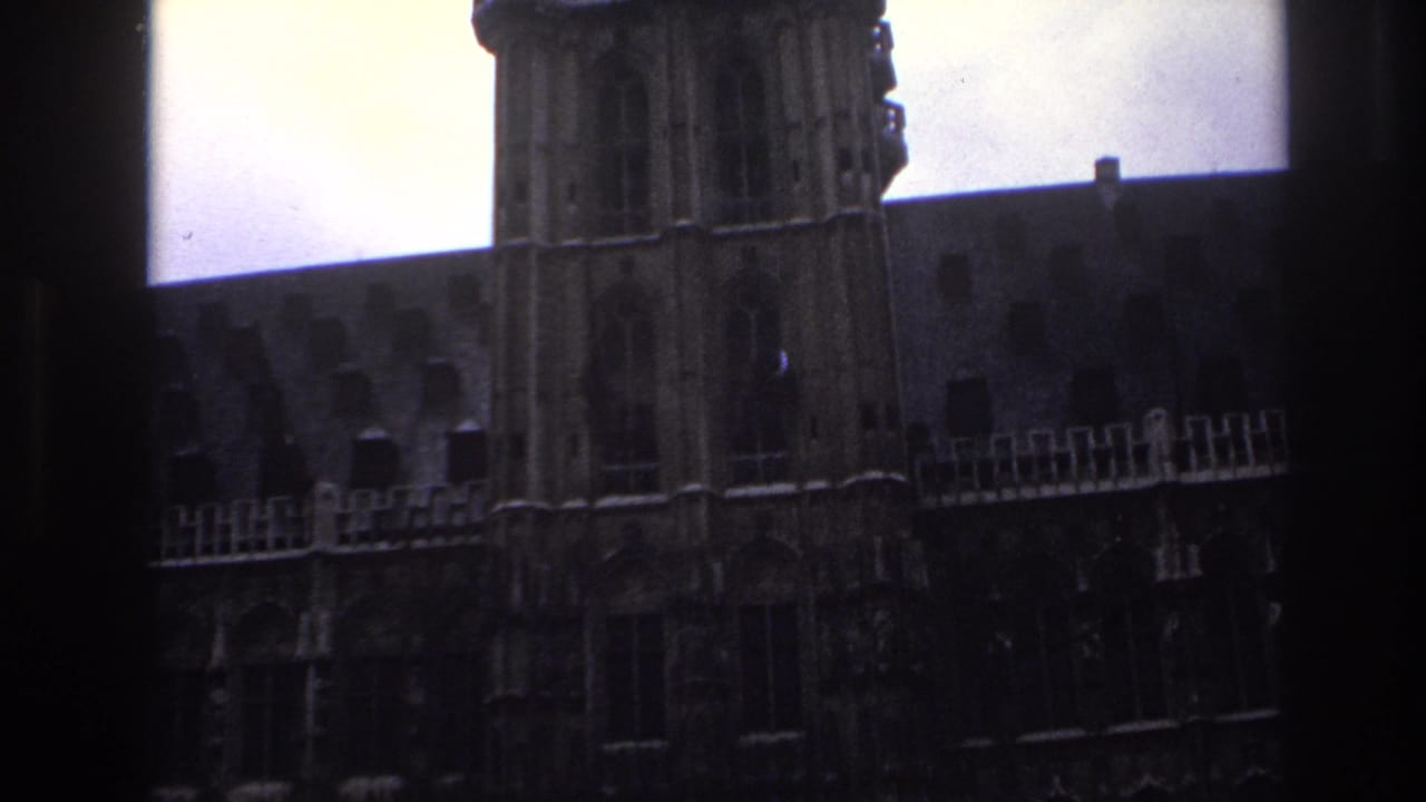 1967 Paris home-movie frame showing a historic stone facade viewed through dark window mullions.