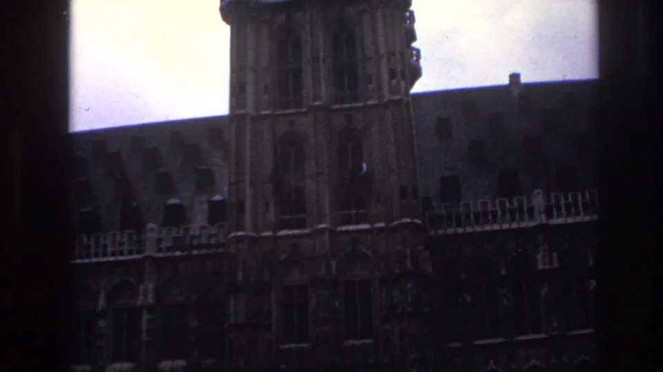 1967 Paris home-movie frame showing a historic stone facade viewed through dark window mullions.