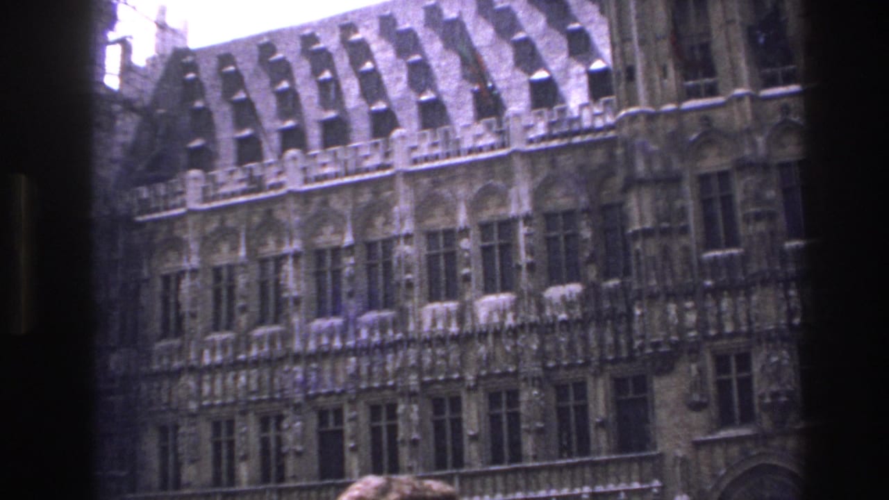 1967 Paris home-movie frame showing an ornate historic facade, steep roofline, arched windows, and partial scaffolding viewed through a dark frame.