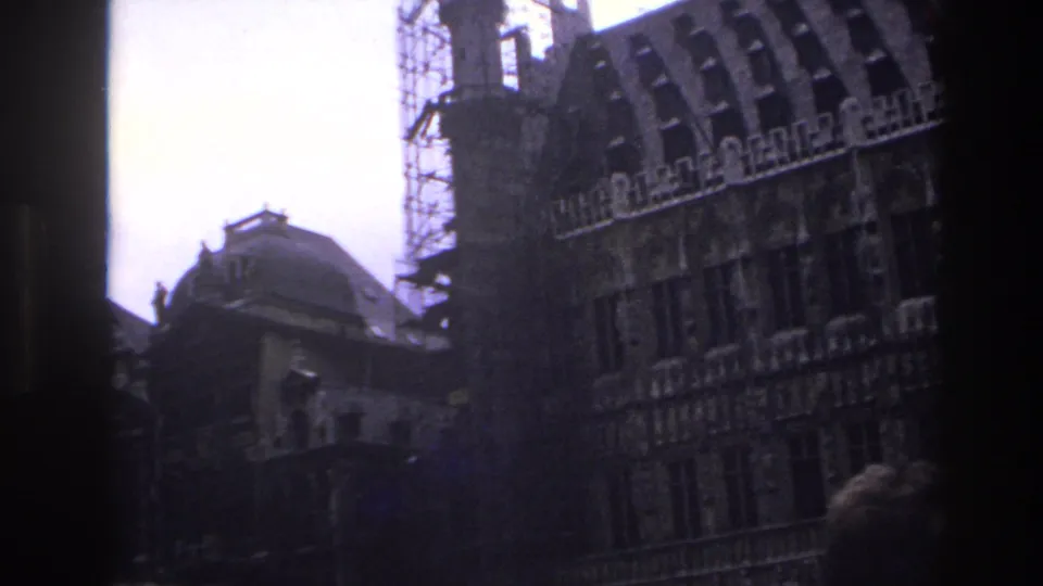 1967 Paris frame showing a historic facade under restoration, a distant domed roof, dark window framing, and a partial foreground head.
