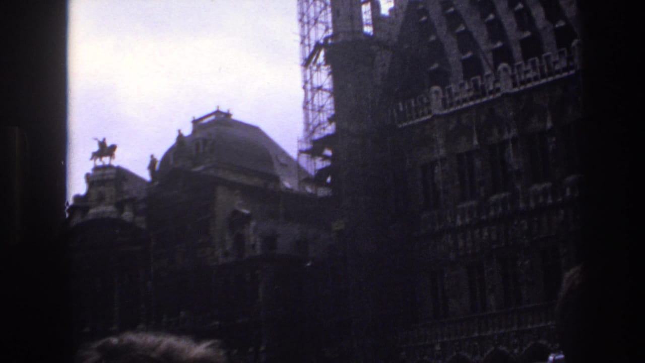 1967 Paris home-movie frame looking upward at shadowed historic rooftops, a domed roof, scaffolding, and an equestrian statue.
