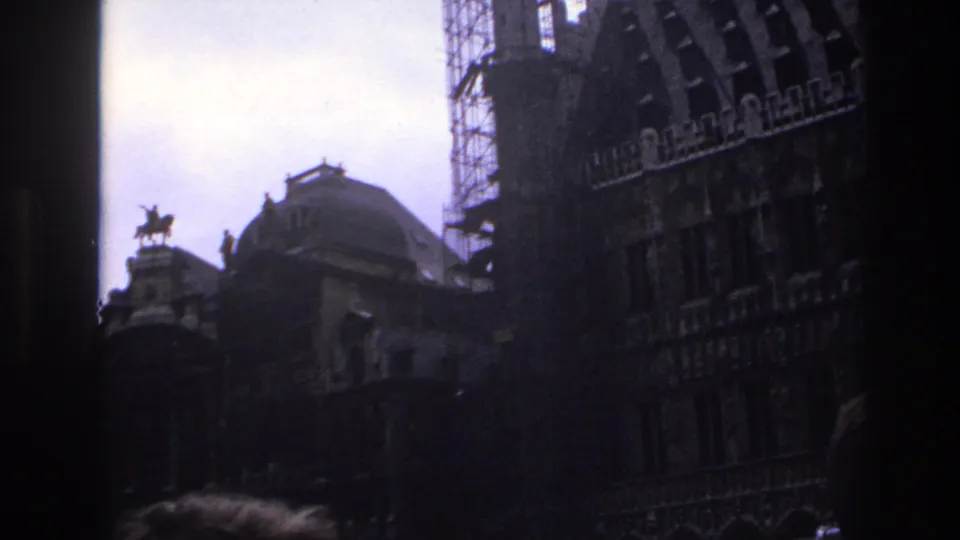 1967 Paris home-movie frame looking upward at shadowed historic rooftops, a domed roof, scaffolding, and an equestrian statue.