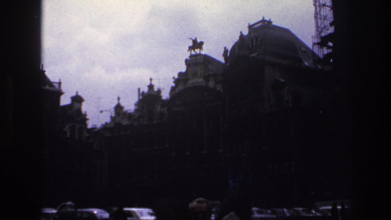 1967 Paris home-movie frame showing grand historic buildings, a roofline statue, cars, and silhouetted people in the foreground.