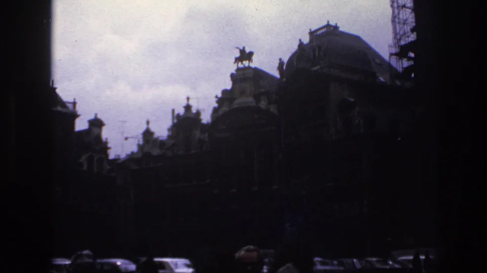 1967 Paris home-movie frame showing grand historic buildings, a roofline statue, cars, and silhouetted people in the foreground.