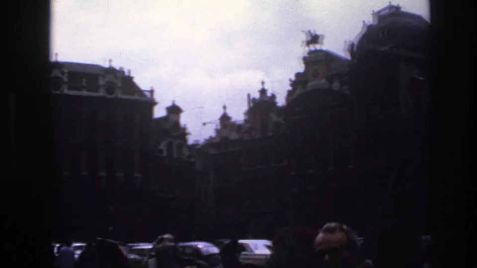1967 Paris street view with historic facades, roof sculptures, cars, and partial pedestrian faces at the bottom edge.