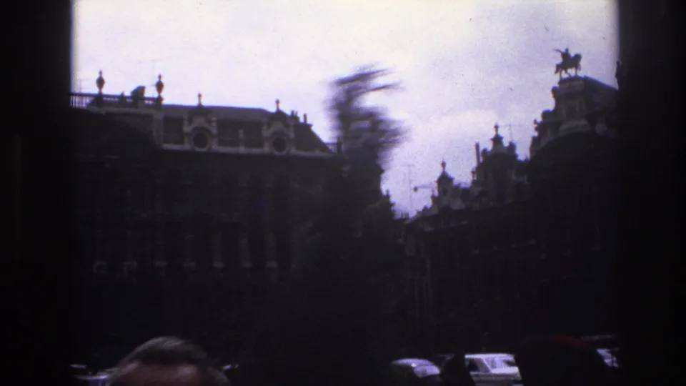 Handheld 1967 Paris frame with motion blur, ornate rooftop details, an equestrian statue, cars, and a partial face near the lower edge.