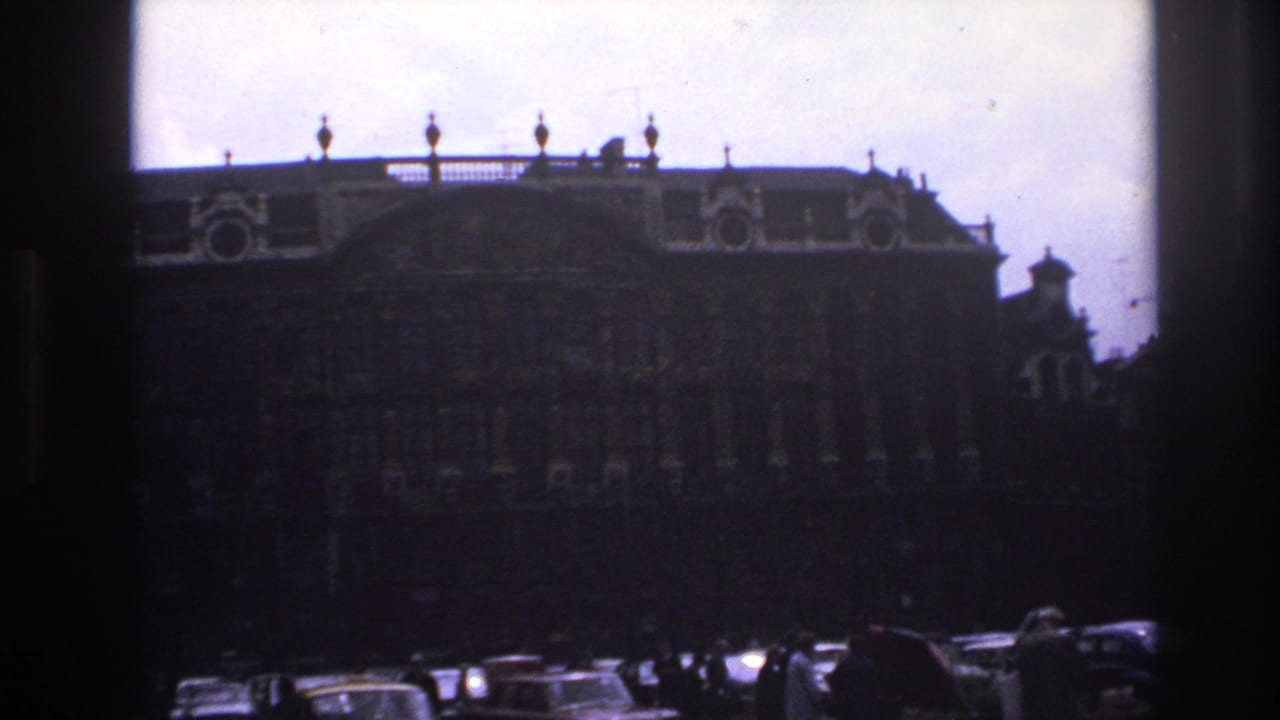 1967 Paris street view of an ornate historic facade seen through dark film borders, with traffic and pedestrians along the square.