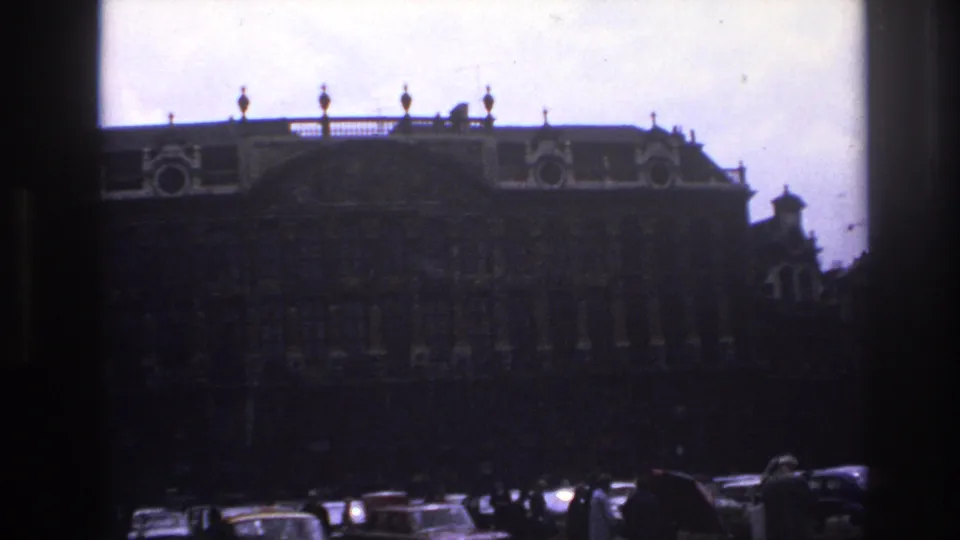 1967 Paris street view of an ornate historic facade seen through dark film borders, with traffic and pedestrians along the square.