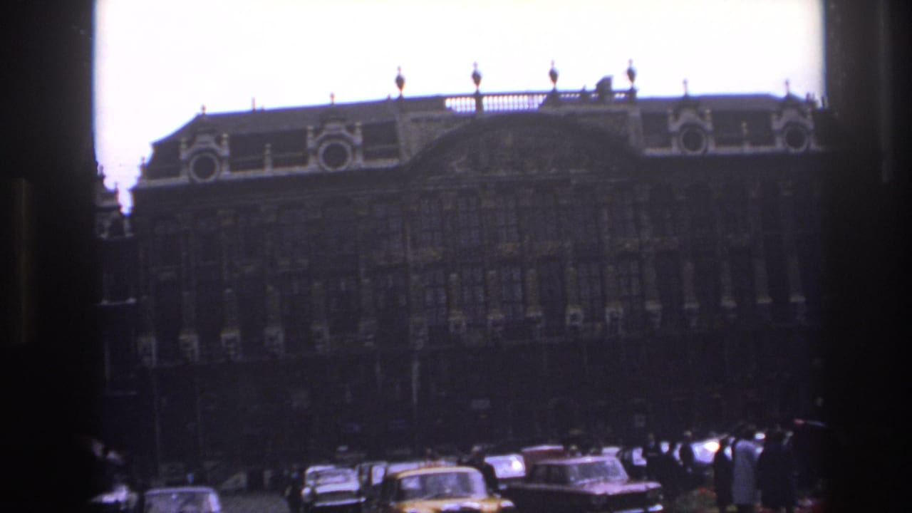 Historic facade across a busy square with several classic cars in the foreground.