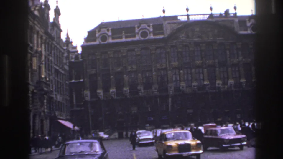1967 Paris street scene with a yellow taxi, classic sedans, pedestrians, and a large historic building ahead.