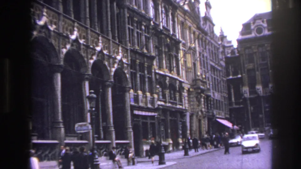 1967 Paris travel-film frame showing a tilted view of historic stone buildings, pedestrians, and a white car on the street.