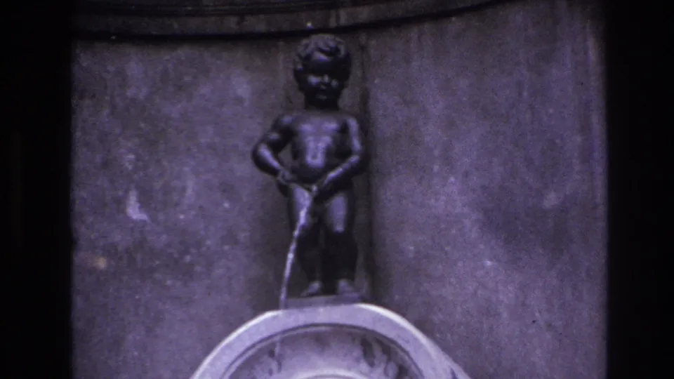 1967 8mm travel frame showing a small boy-like fountain statue with water flowing downward against a dark stone wall.