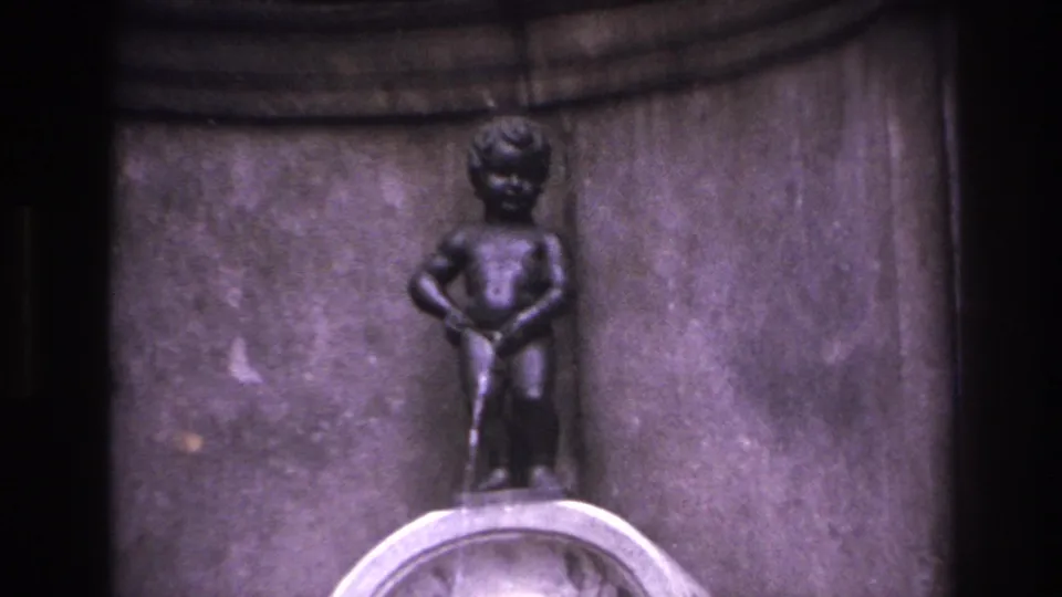 1967 8mm travel frame showing a close view of the small bronze fountain figure and pale basin against carved stonework.