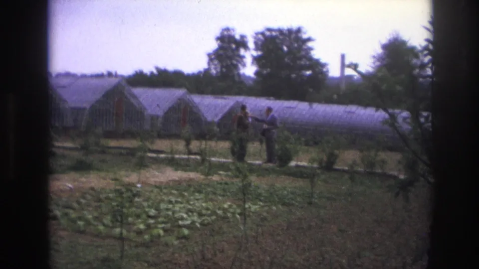 1967 Paris home-movie frame of two adults talking in a garden, with one possibly holding a small child or bundle.