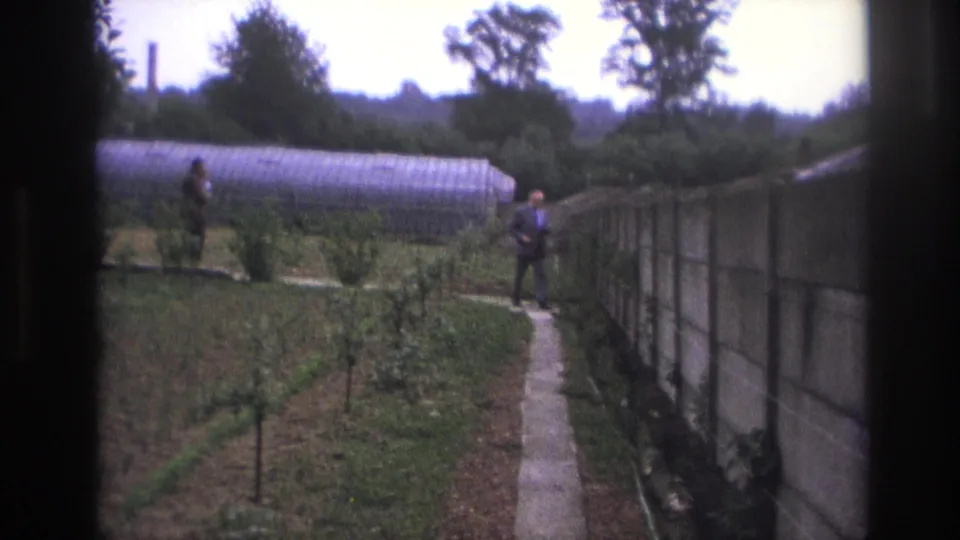 Paris, France, 1967 frame showing a suited man on a narrow path with another man near an arched greenhouse.