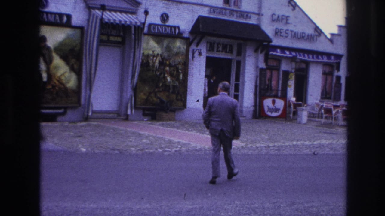 A suited pedestrian crosses a Paris street toward a cinema and cafe frontage, with French signage, poster displays, and outdoor seating visible.