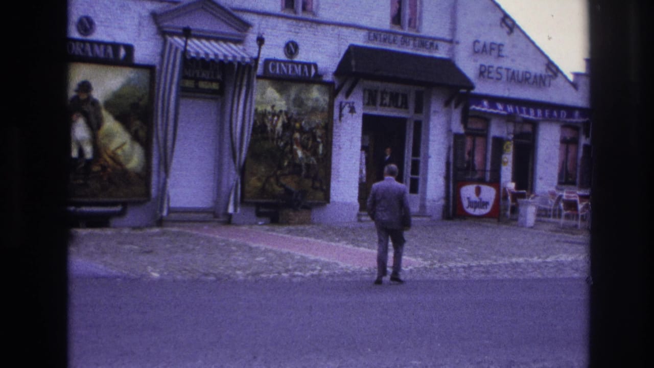 A man stands in the street facing a cinema entrance beside a cafe.