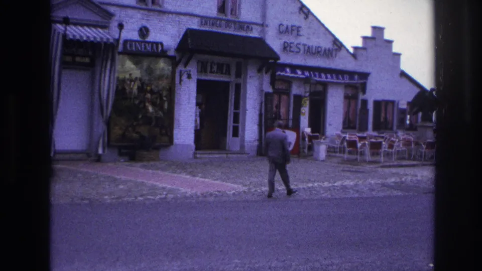 1967 Paris home-movie frame showing the man walking along the street past outdoor cafe seating next to the cinema.